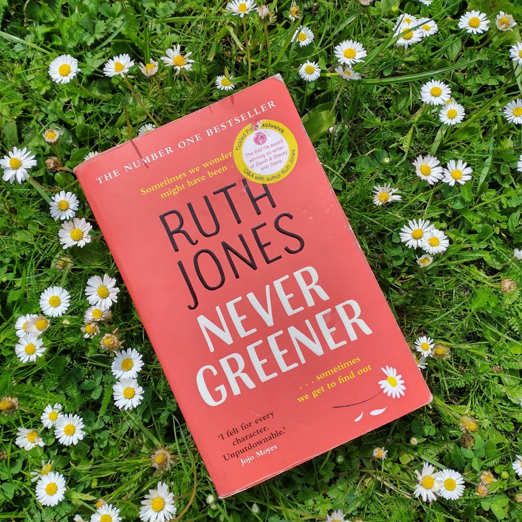 The book Never Greener by Ruth Jones lying on a patch of green grass and daisies which echo the daisy on the book cover.